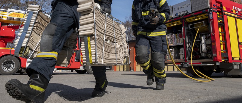 Två brandmän som bär slangar. I bakgrunden syns två brandbilar.